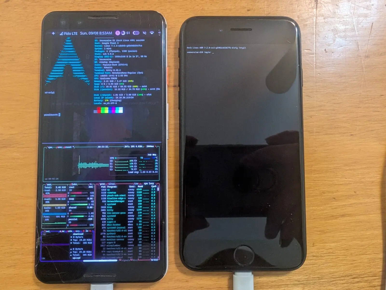 A powered Pixel 3 running SouveraineOS beside an iPhone 7 at a login prompt, both cabled on a wooden workbench.